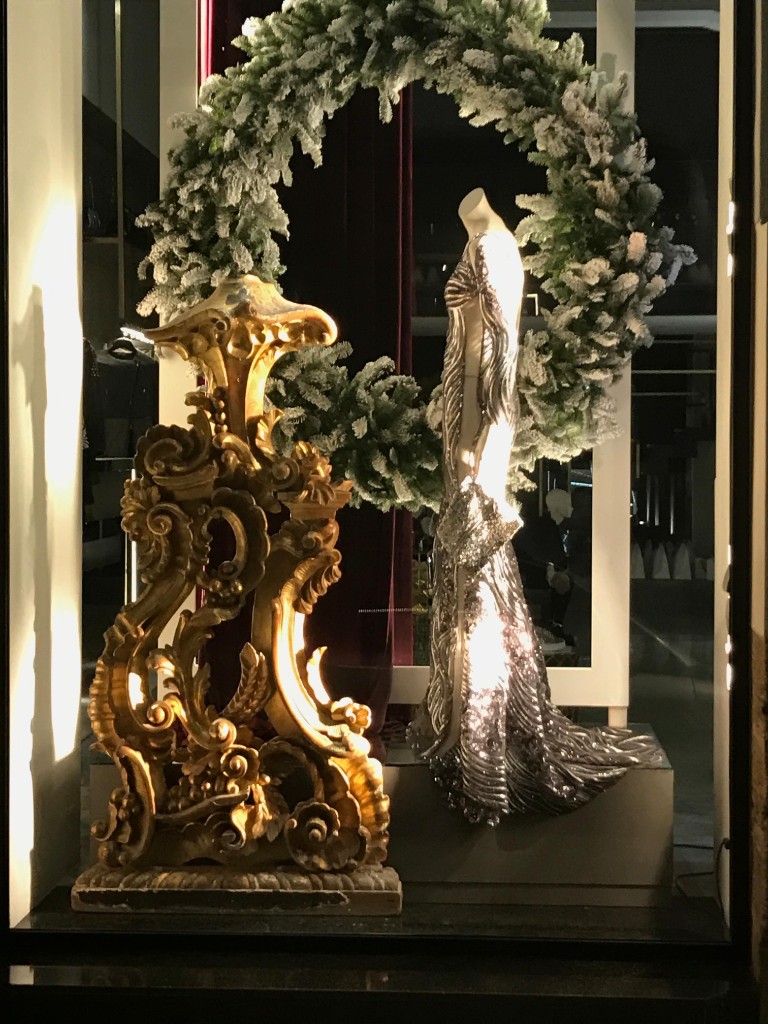 Vetrina del concept store con abito argento su manichino, cornice barocca dorata e ghirlanda
